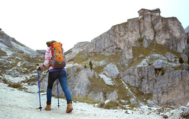 Escursionista con zaino e bastoncini cammina verso una baita in montagna.