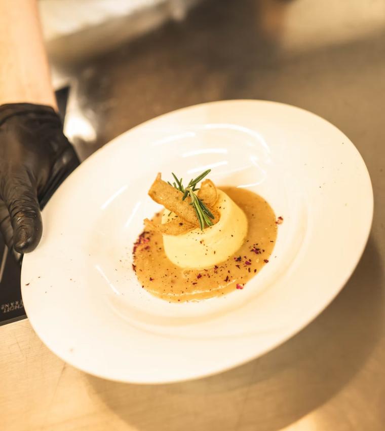 Piatto elegante con purè, salsa, decorato con crostini e rosmarino.